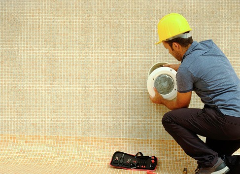 Electrician with Screwdriver Fixes Light Bulb in an Empty Swimming Pool Under Construction