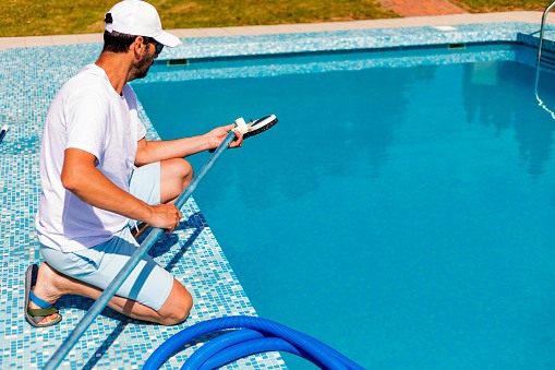 A Man Is Cleaning the Swimming Pool with a Vacuum Cleaner.